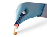 Activon Manuka Honey tube being poured out by hand wearing blue glove. Shows stream of honey coming from tube and resting on backdrop.